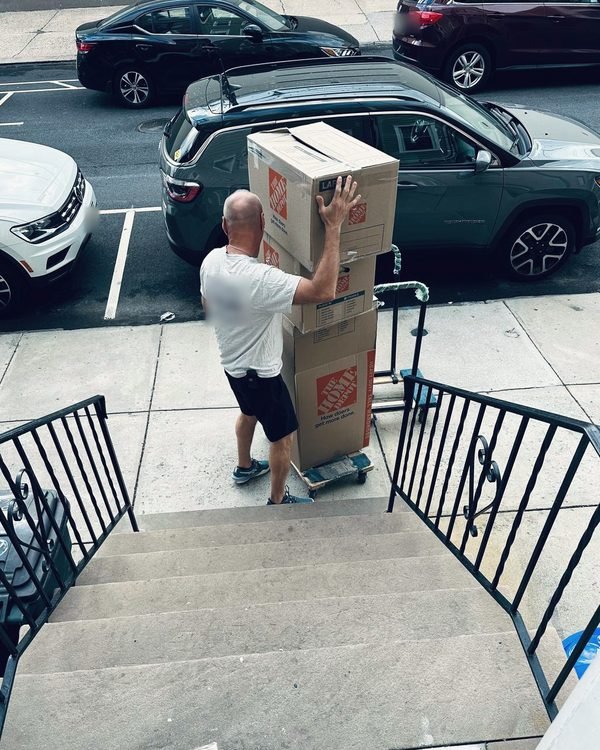 A mover taking a stack of boxes down a front stoop to the sidewalk