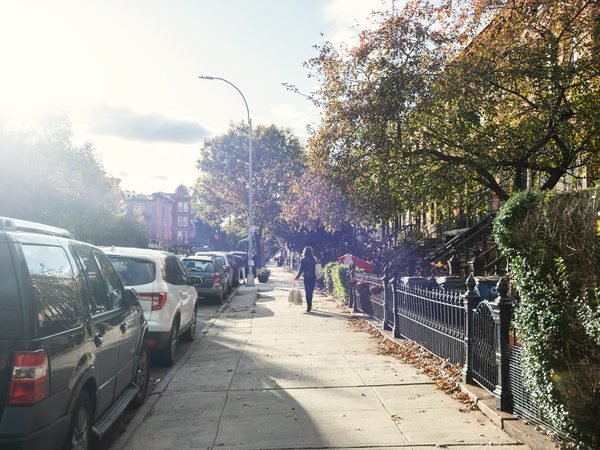 A sunny Brooklyn sidewalk in autumn with brownstones behind iron fences