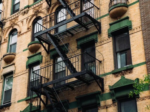 A yellow-brick walk-up with a black fire escape and green trim